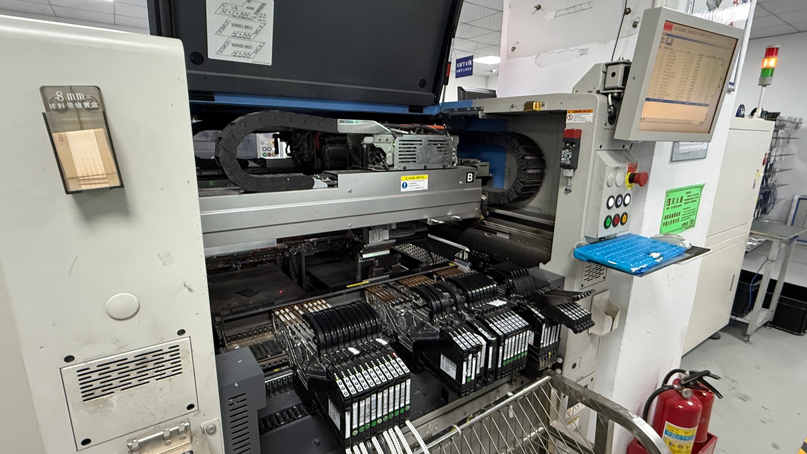 SMT placement machine with component tape feeders and an adjacent control screen in a PCB assembly factory