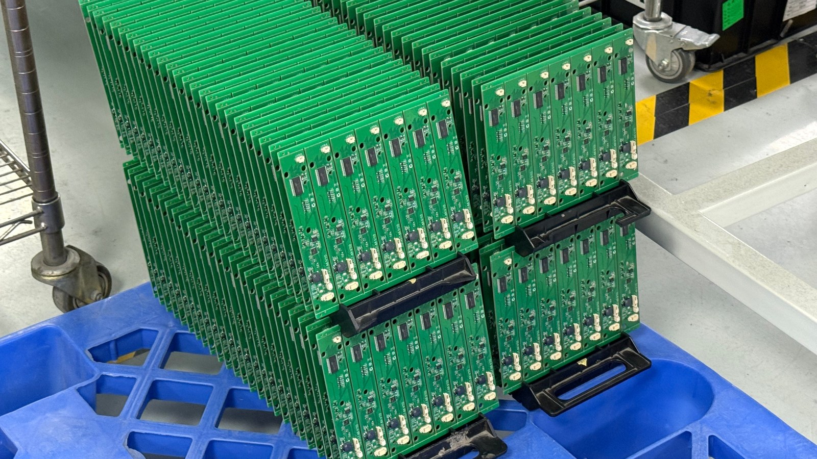 Assembled green circuit boards arranged vertically in black carriers over a blue factory bin