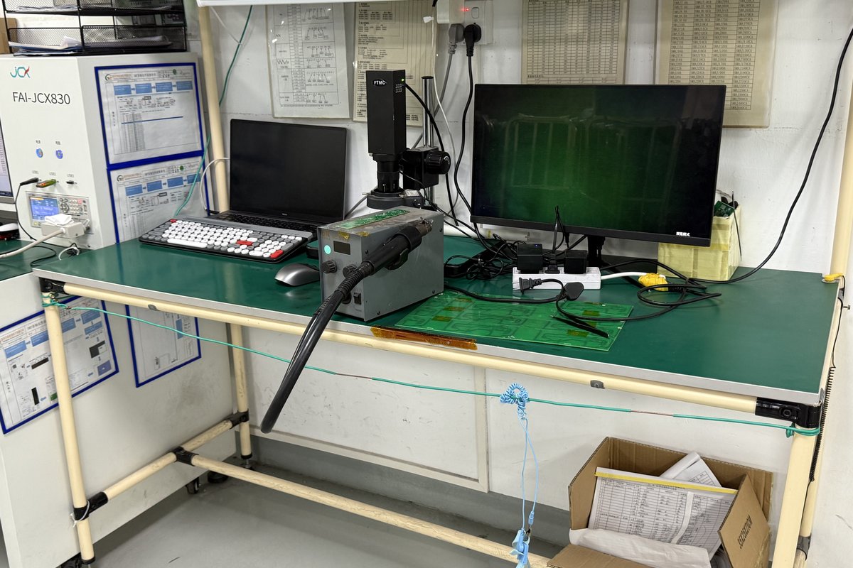Real factory photo of a PCB inspection workstation with a board under a camera and monitoring equipment