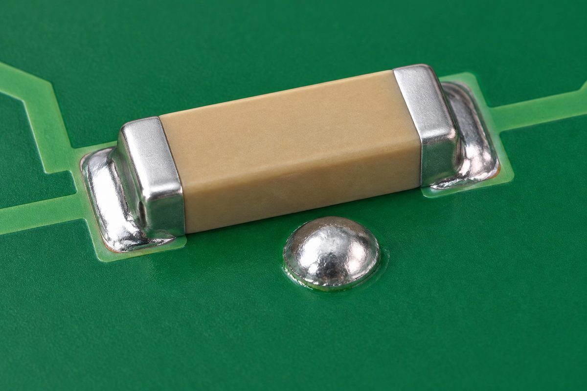 Conceptual flat chip capacitor with a separate rounded silver deposit beside its body and distinct soldered end pads